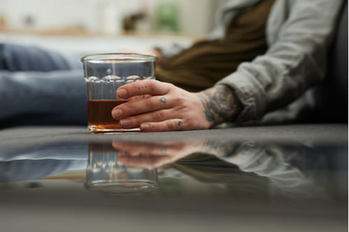 Мужчина со стаканом алкоголя лежит на полу